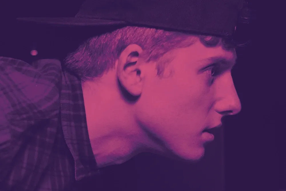Purple-tinted portrait of a man wearing a cap.