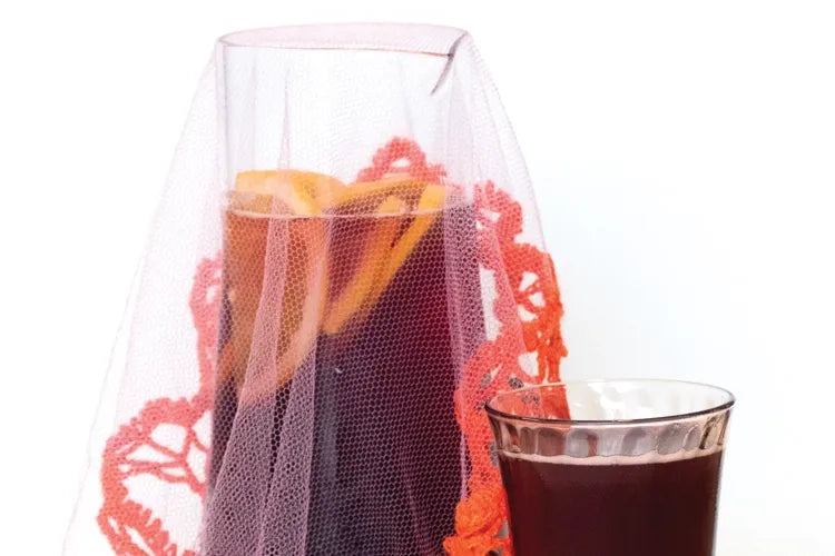 A close crop of a sangria pitcher and glass with citrus garnish.
