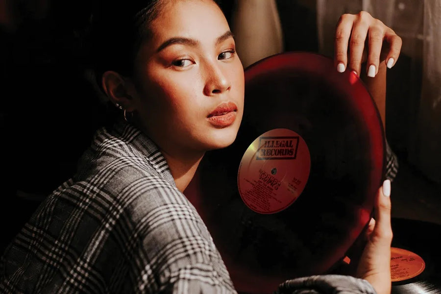 A person in a checked jacket holds a vinyl record beside their face.