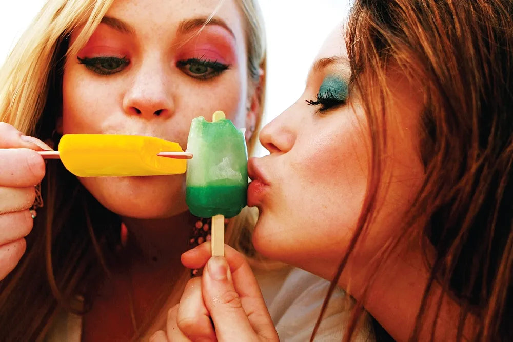 Two people taste yellow and green ice pops.