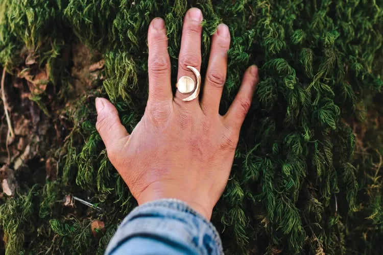 A close-up of a ringed hand resting on moss-covered bark.