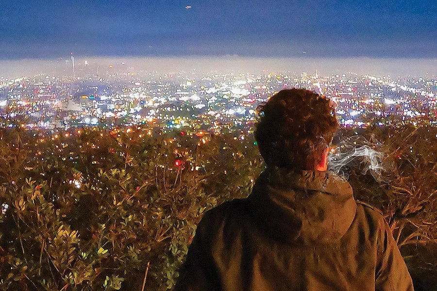 A smoker looks across the illuminated Los Angeles skyline at night.