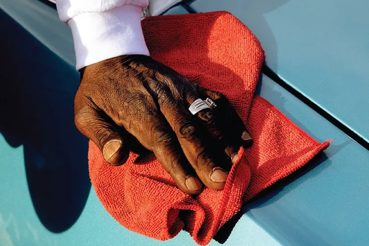 Close-up of a ringed hand and red cloth polishing a glossy blue car.