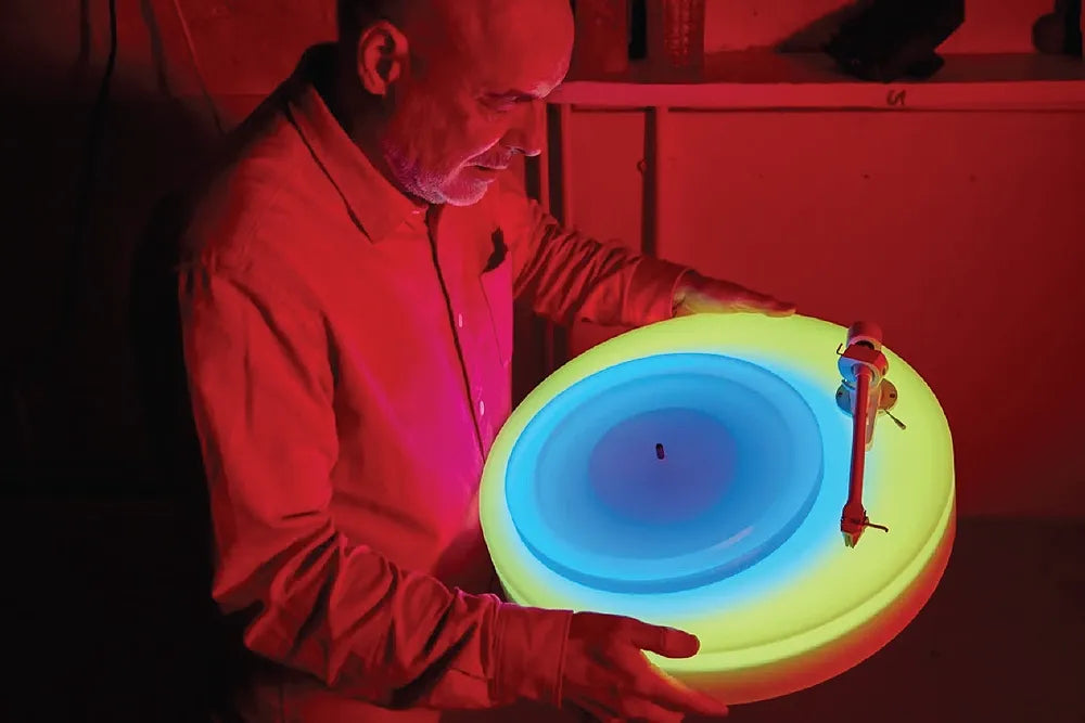 A person holds a circular turntable glowing in blue, green and yellow.