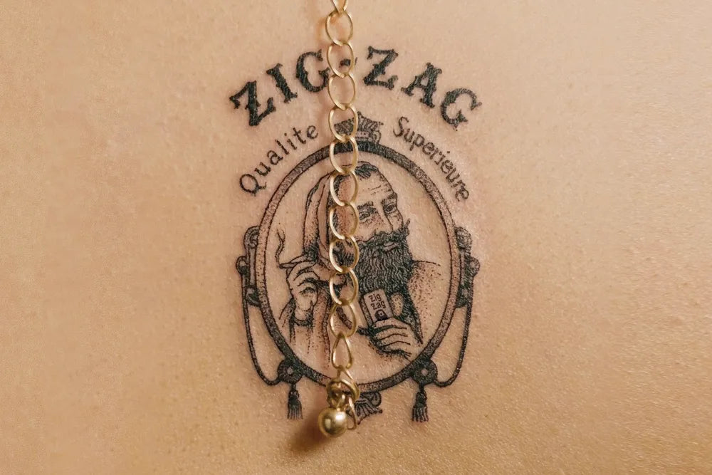 A Zig-Zag logo tattoo beneath a gold necklace.