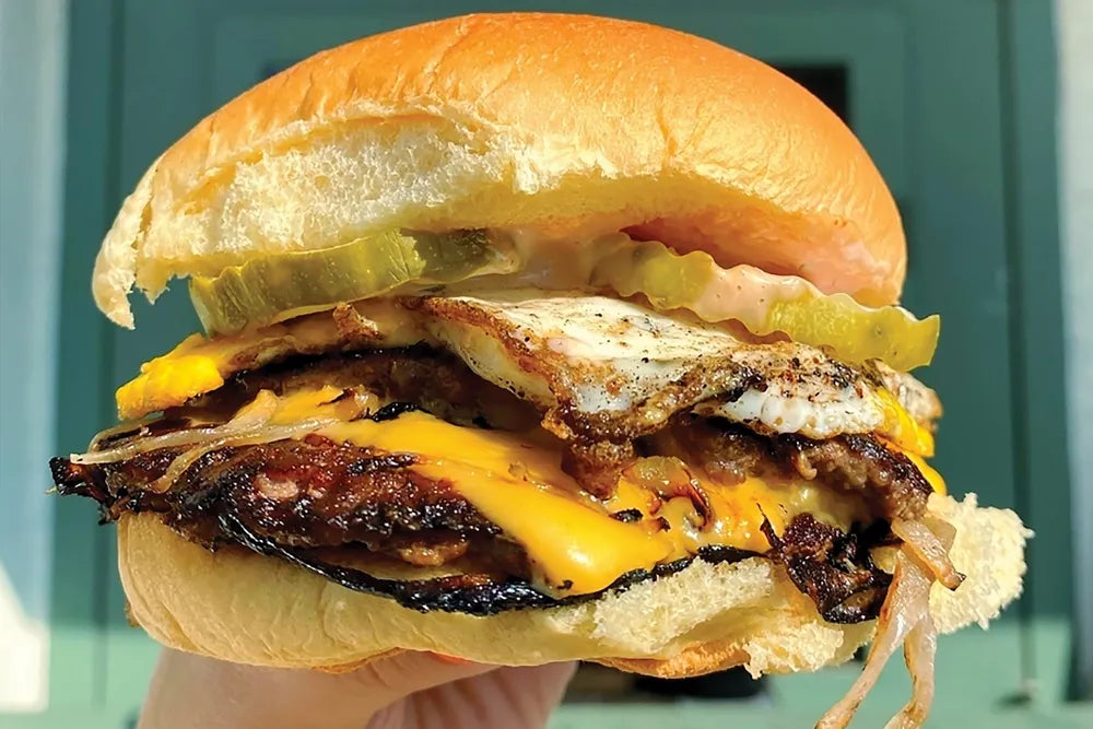 A close-up of a cheeseburger topped with a fried egg and pickles.