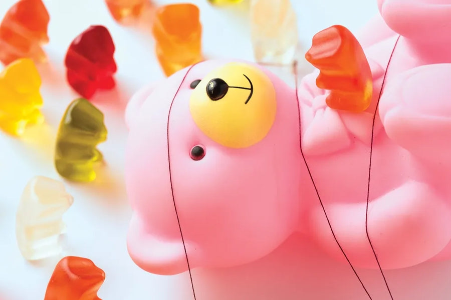 Colorful gummy bears surround a large pink toy bear.