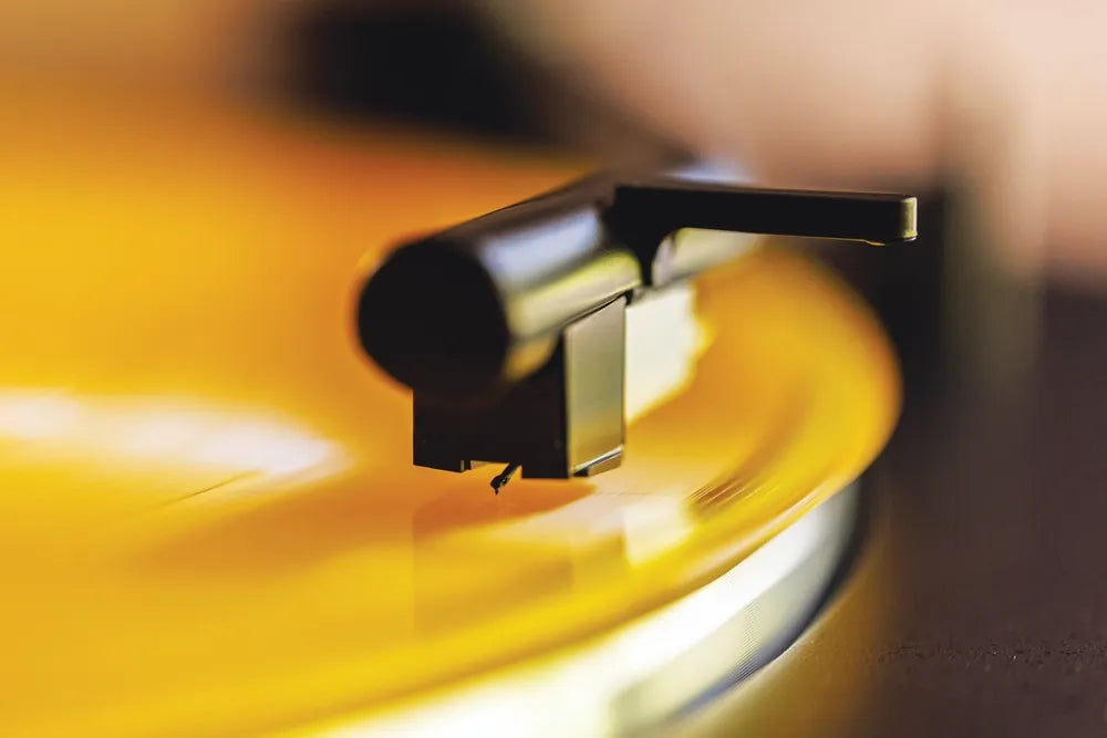 A close-up of a stylus playing a yellow vinyl record.