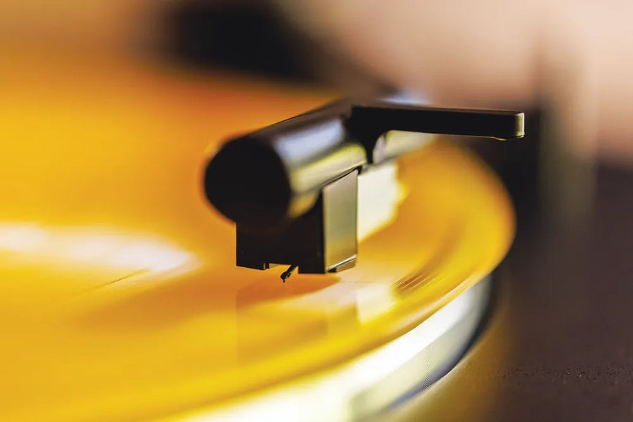 A close-up of a stylus playing a yellow vinyl record.