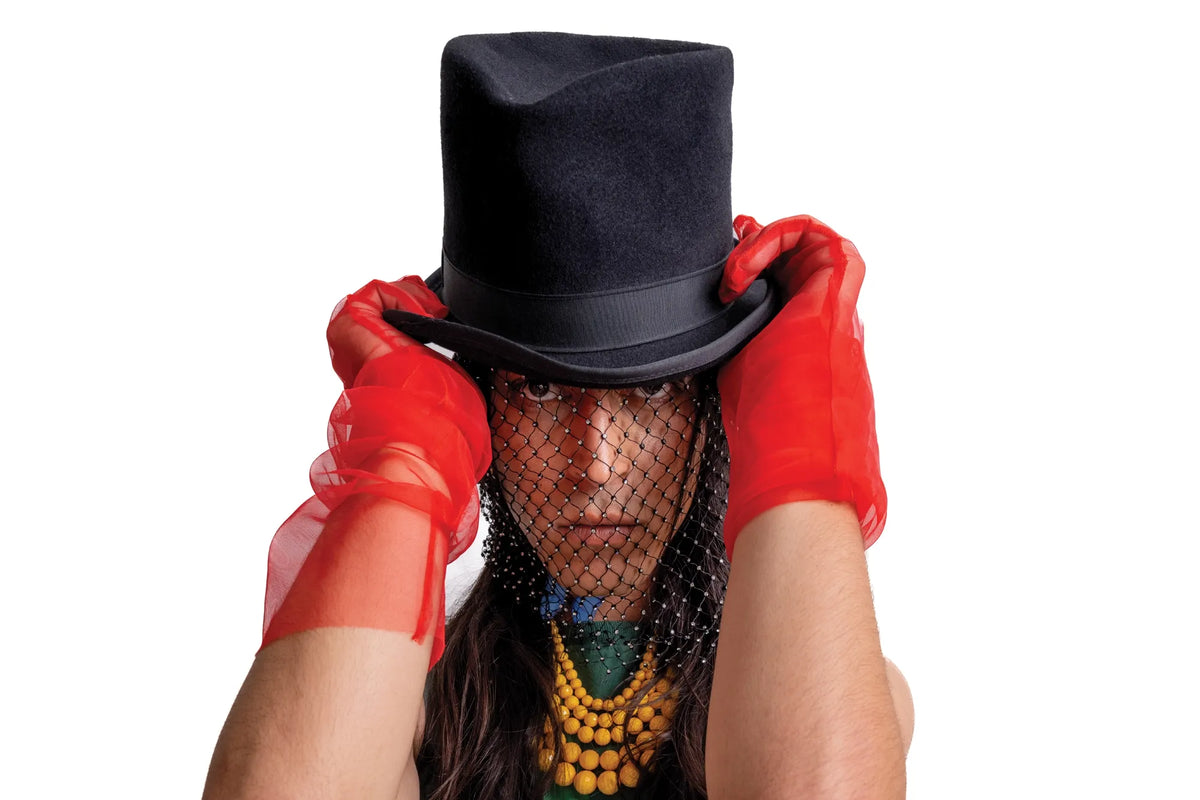 A model wears a black top hat, netted veil, red gloves and layered necklaces.