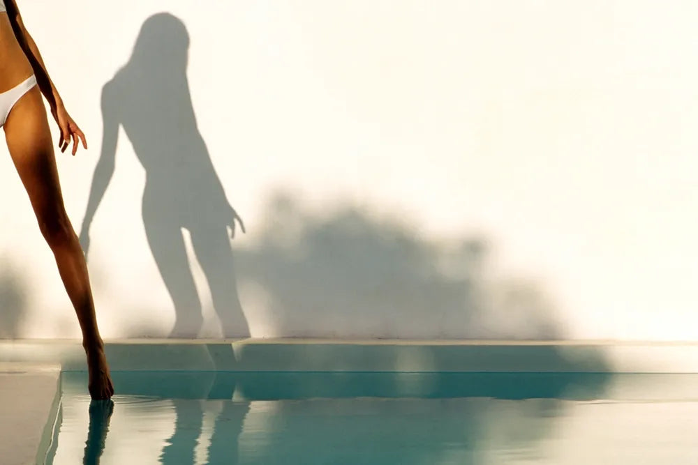 A swimmer's legs and long shadow beside a swimming pool.