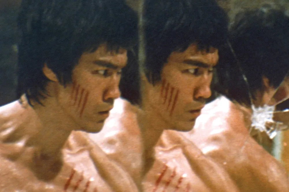 A close-up of Bruce Lee and his reflections in cracked mirrors.