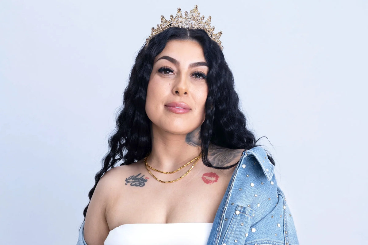 A woman wearing a crown, layered necklaces and a denim jacket.